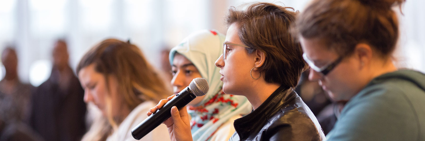 Female student holds microphone and speaks to audience